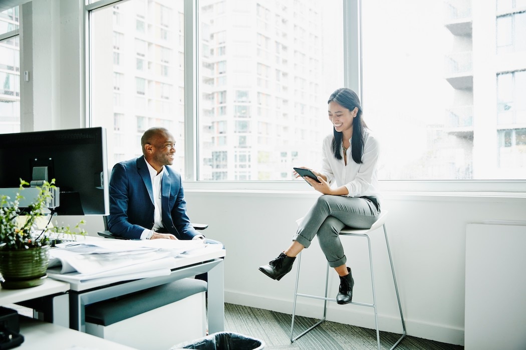 Smiling businesswoman discussing project on digital tablet with coworker at office workstation 