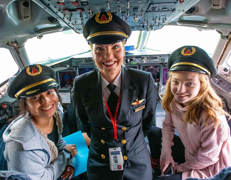 Piloto mujer en cabina de vuelo con dos participantes del programa