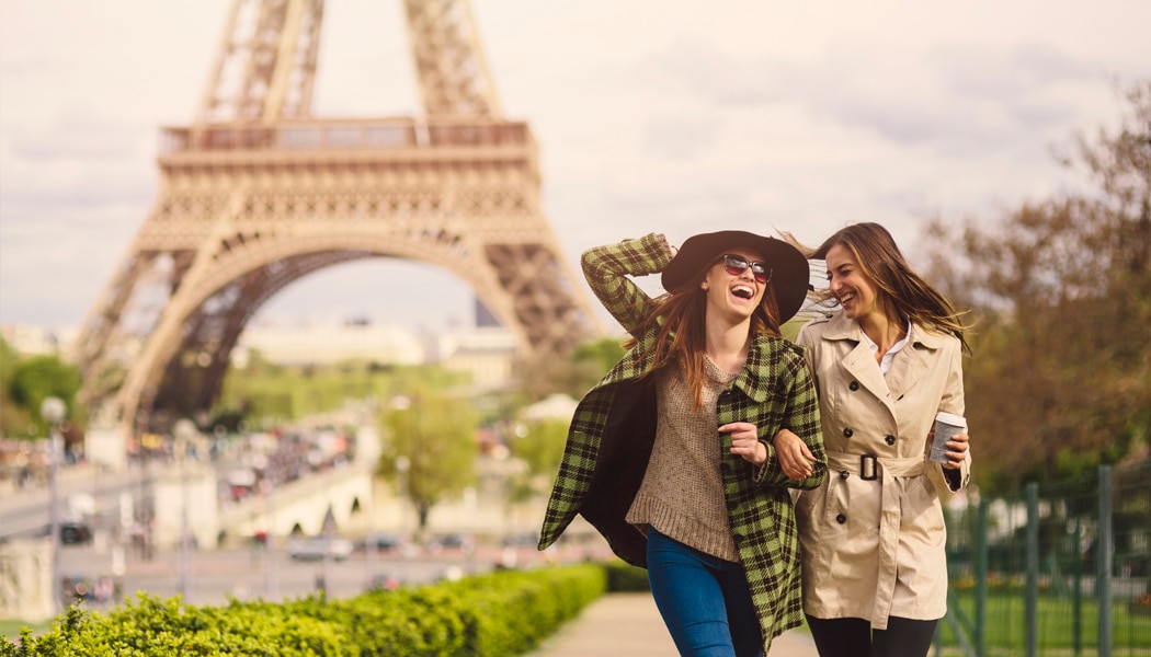 Two women laughing while walking in front of the Eiffel Tower