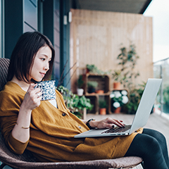 Mujer en un patio usando su computadora portátil y disfrutando de un café