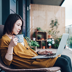 Mulher em um pátio usando seu laptop e tomando café