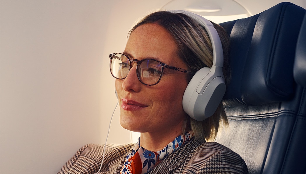 Woman seated on aircraft with headphones listening to audio