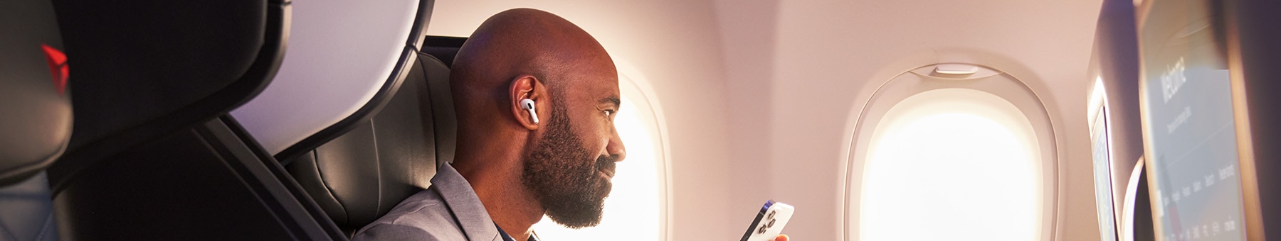Man sitting in First Class Seat with ear pods smiling