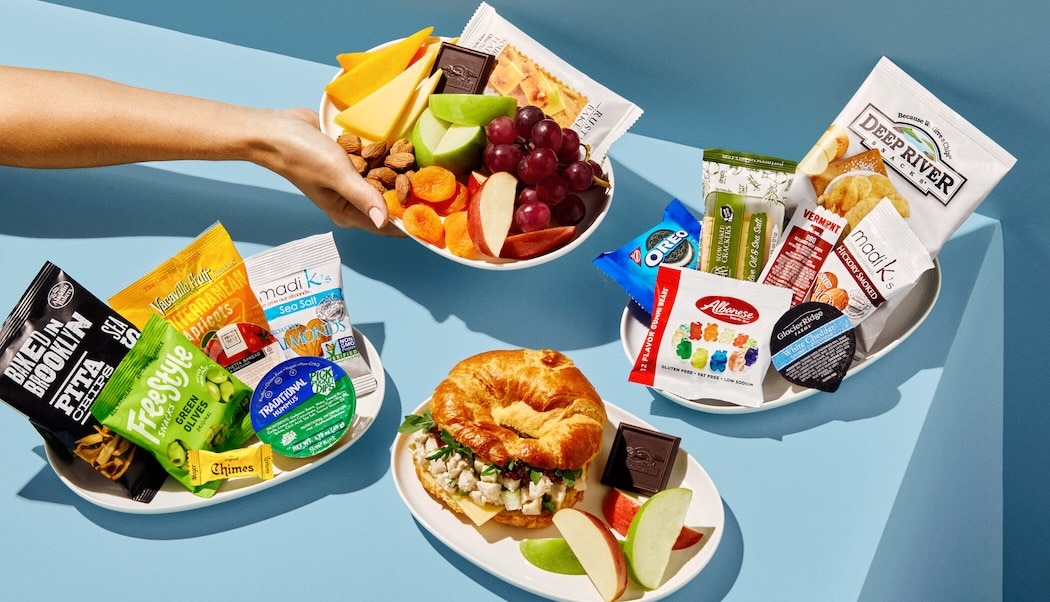 An assortment of onboard snack-box items, including fruit, crackers, nuts and chips