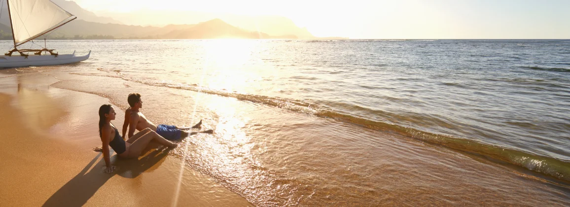 Two people relaxing on beach at sunset by ocean.