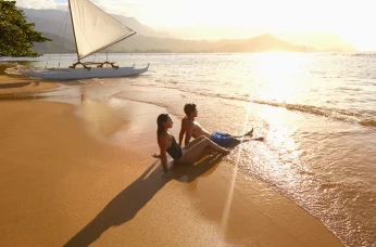 Two people relaxing on beach at sunset by ocean.