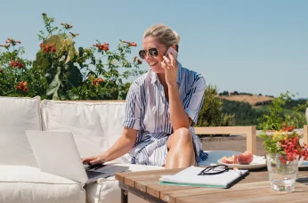 Person using laptop and phone in an outdoor setting, representing flexible work and travel lifestyle.
