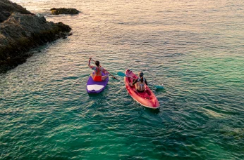 Two people kayaking near rocky shore, representing Delta SkyMiles travel experiences.