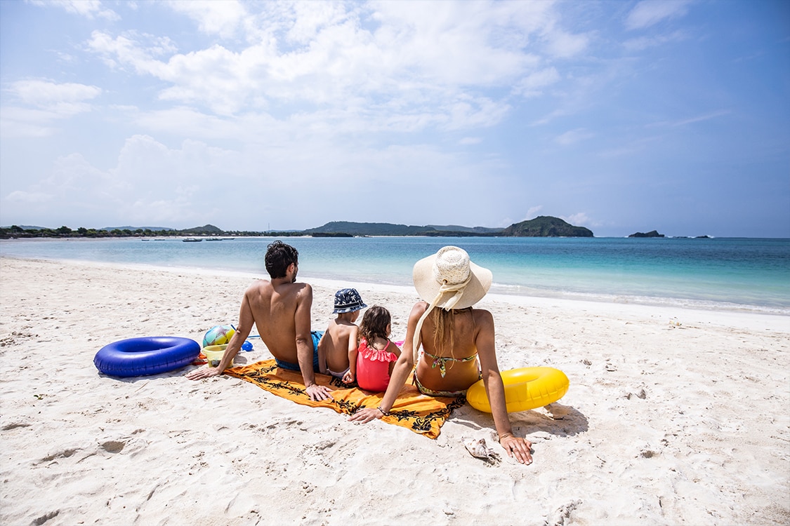 Family of 4 looking out over the water on the beach during a sunny day. 