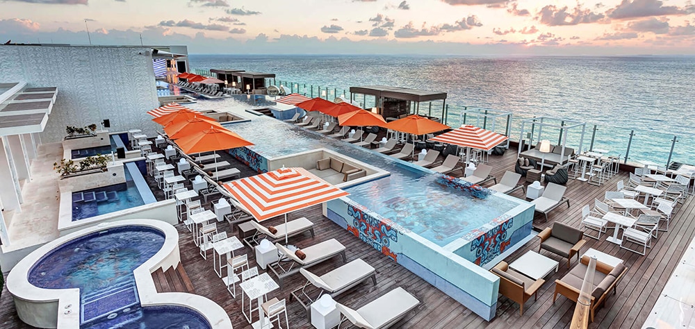 Luxury Cancun resort, rooftop, infinity pool with ocean views, lounge, chairs, and umbrellas. 