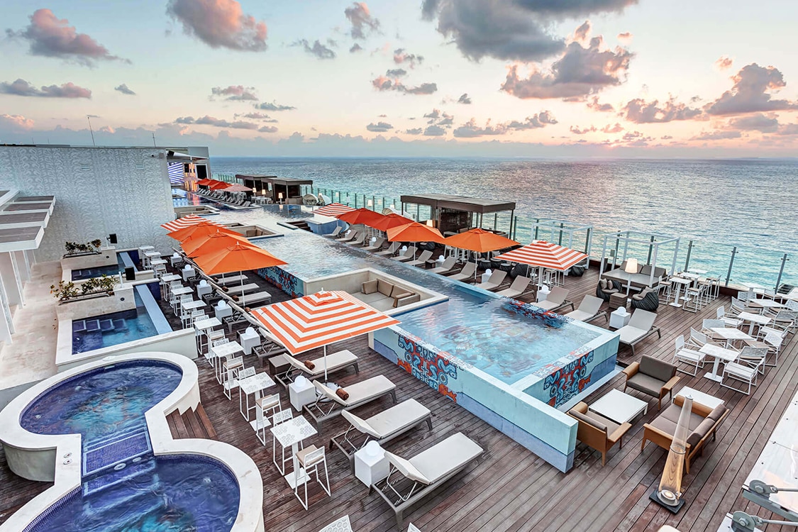 Luxury Cancun resort, rooftop, infinity pool with ocean views, lounge, chairs, and umbrellas. 