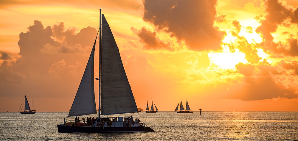 Boats cruising across the ocean at sunset with golden skies. 