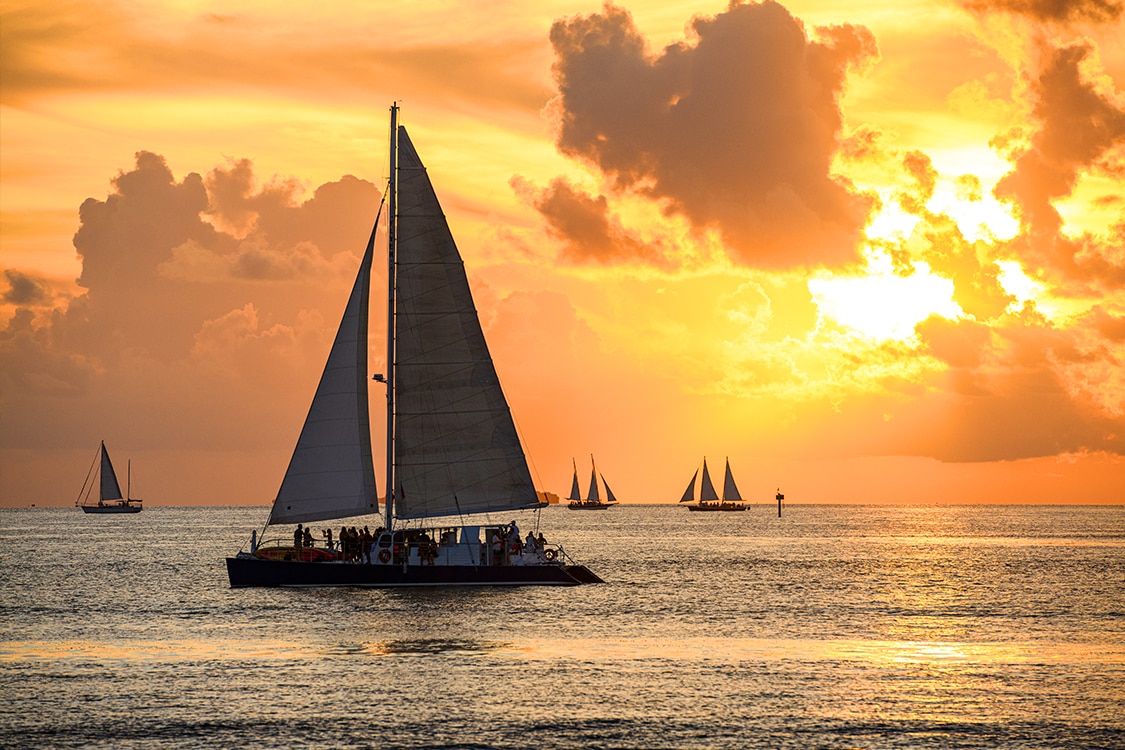 Boats cruising across the ocean at sunset with golden skies. 