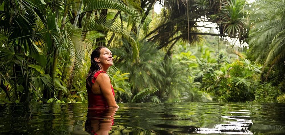 Woman relaxing in a tropical jungle pool surrounded by lush greenery. 