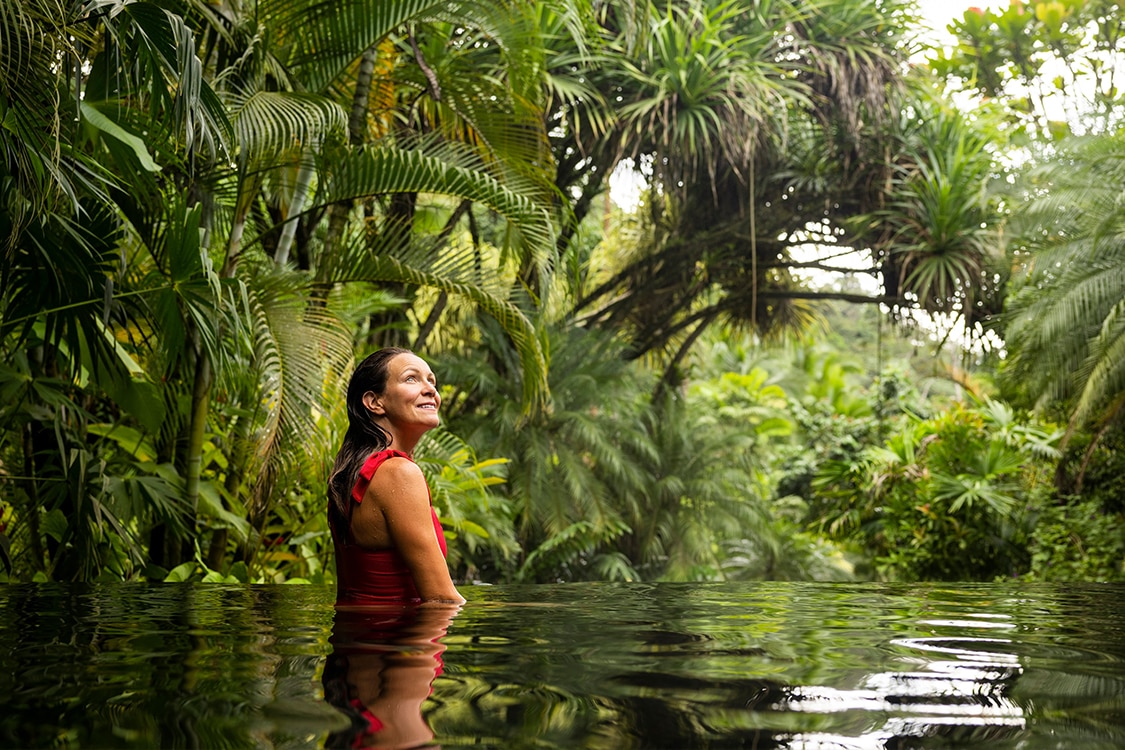 Woman relaxing in a tropical jungle pool surrounded by lush greenery. 