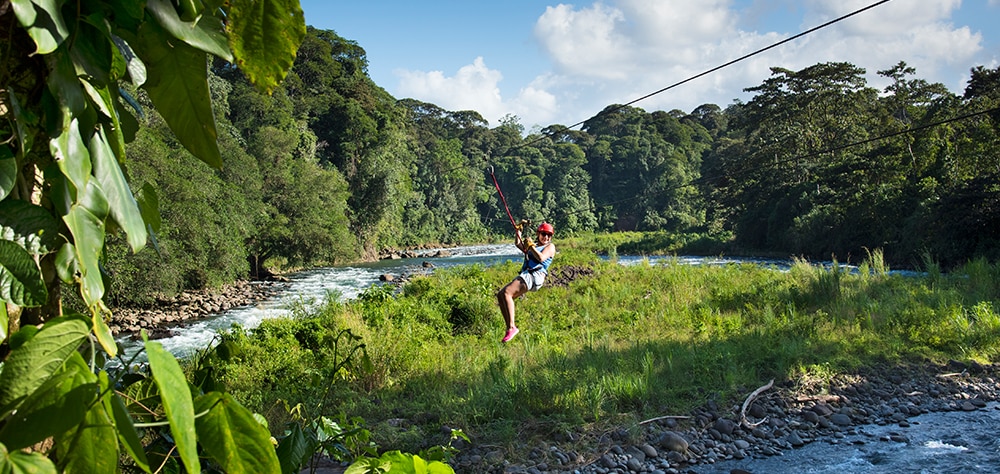 Woman zip lining over a lush river valley surrounded by tropical rainforest. 
