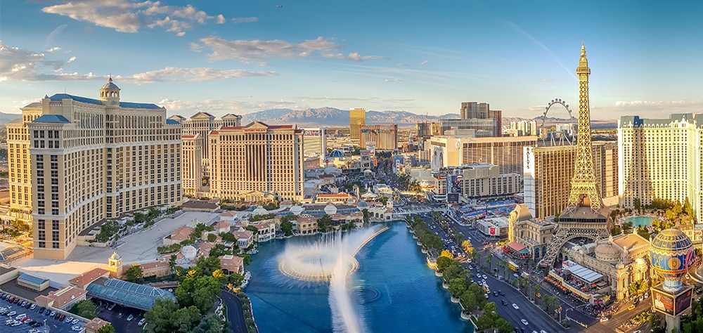 Aerial view of the Las Vegas Strip with hotels, fountains, and city skyline during sunset. 