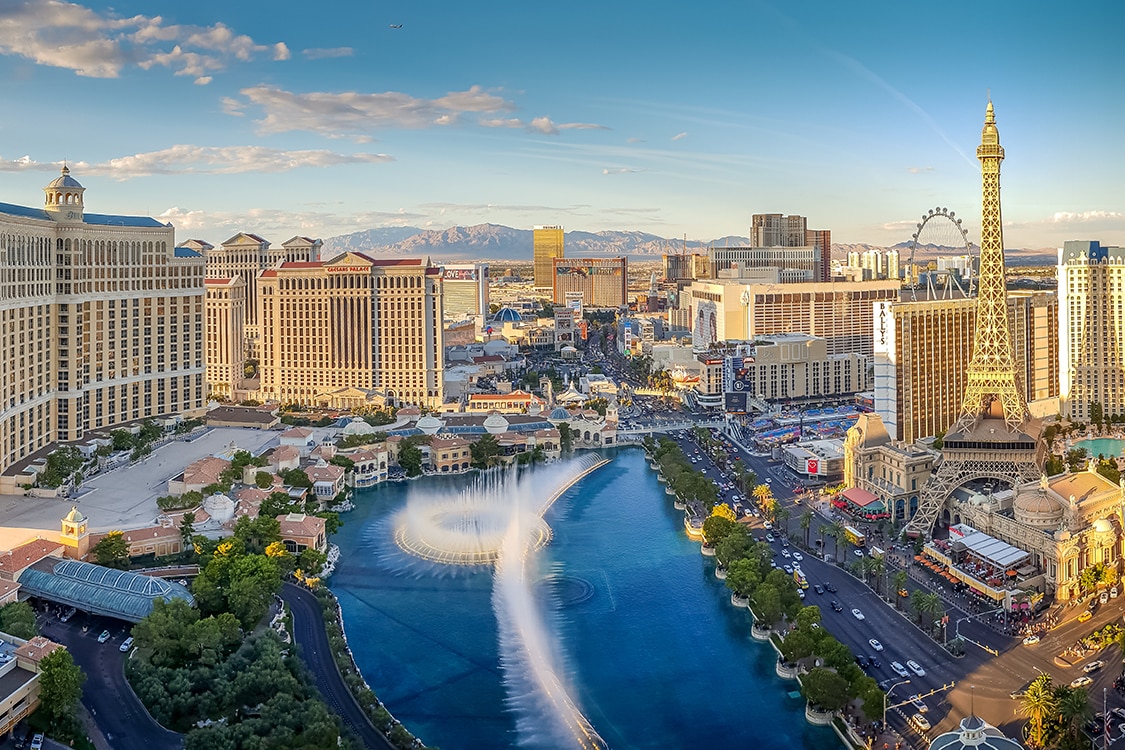 Aerial view of the Las Vegas Strip with hotels, fountains, and city skyline during sunset. 