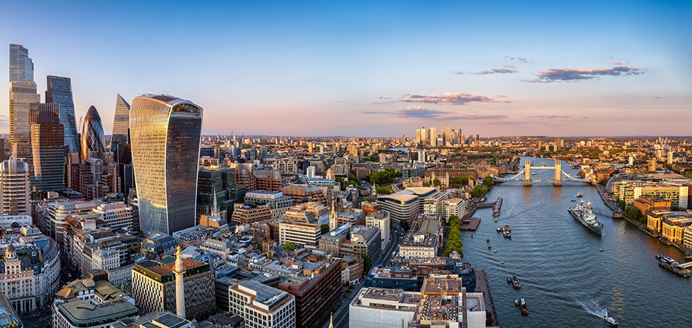 Aerial view of central London featuring the River Thames, Modern skyscrapers, and Tower Bridge. 