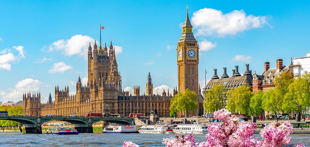 Big Ben and the Palace of Westminster with River Thames, boats, and spring flowers in London on a sunny day. 