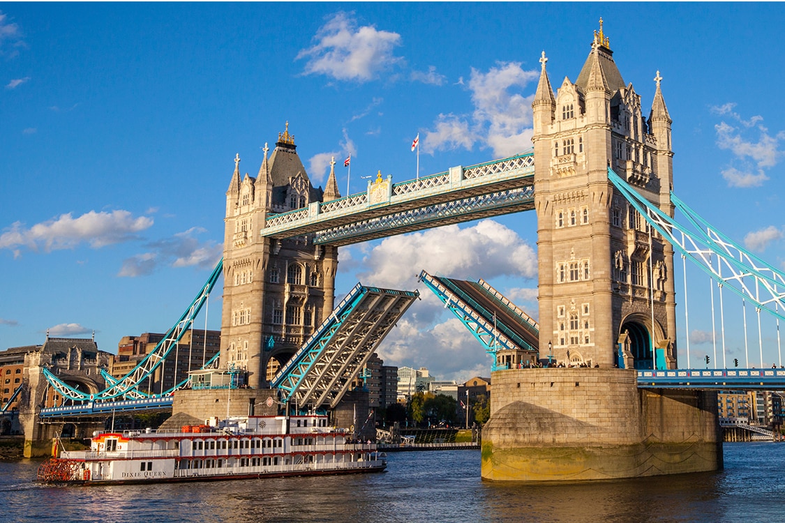 London's Tower Bridge opening over the River Thames with historic towers and blue suspension cables on a sunny day. 