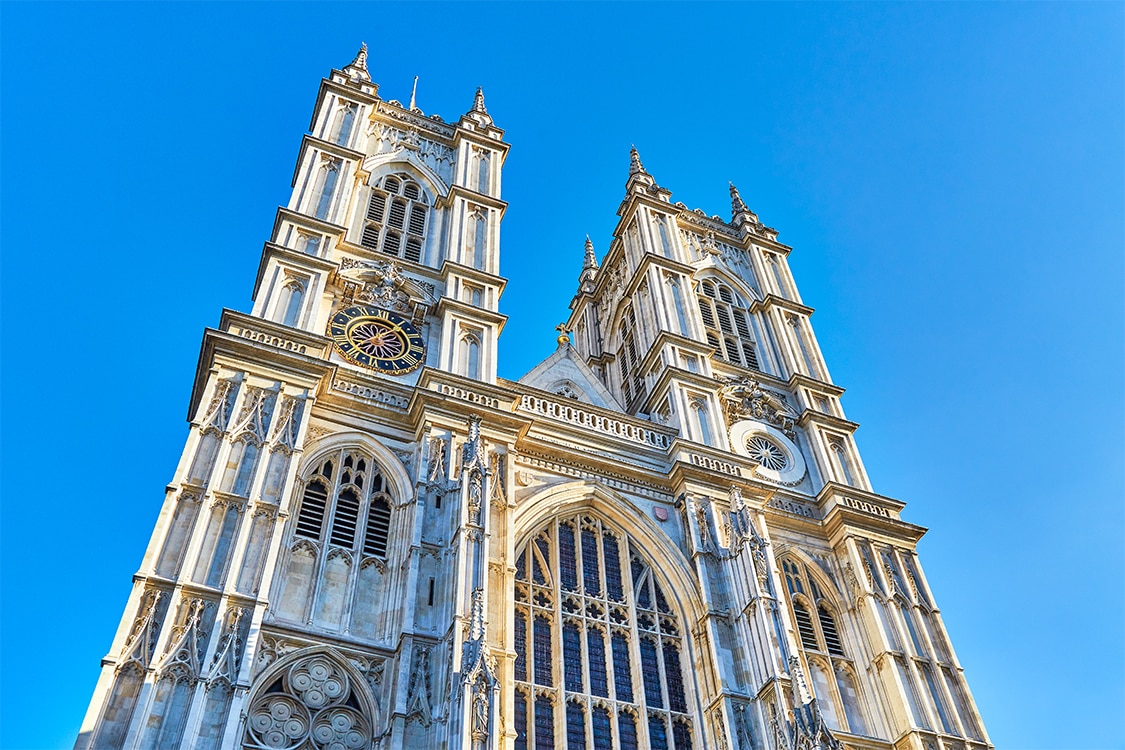 Historic Westminster Abbey in London featuring Gothic stonework, arched windows, and clock tower on a bright sunny day. 