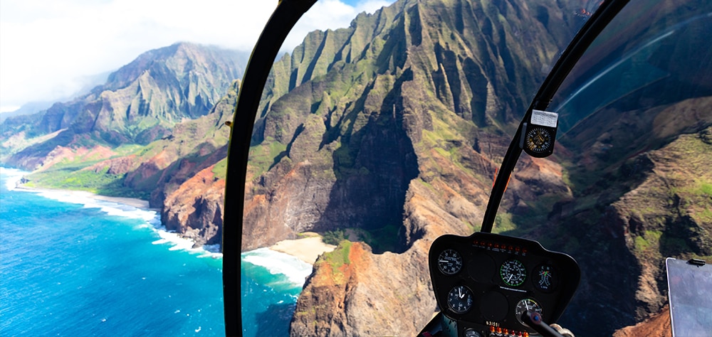 Aerial helicopter view of Maui's rugged coastline, lush green cliffs, and turquoise ocean. 