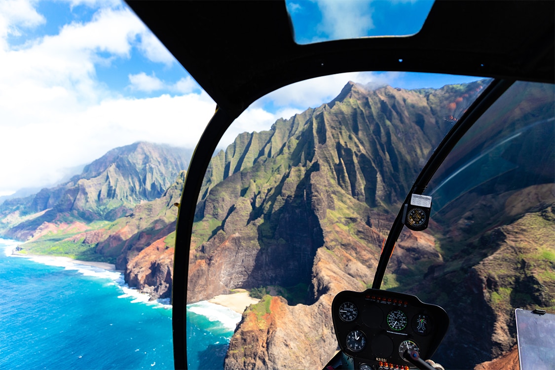 Aerial helicopter view of Maui's rugged coastline, lush green cliffs, and turquoise ocean. 