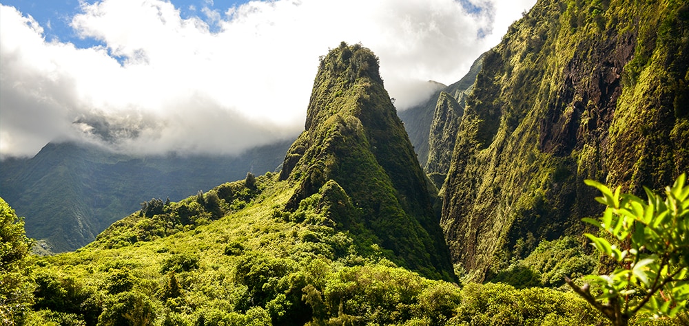Lush green mountain peaks and ridges in Maui surrounded by clouds and tropical vegetation. 