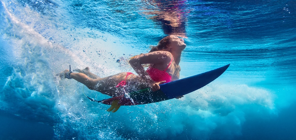 Underwater view of a surfer riding a wave in Maui's clear blue ocean. 