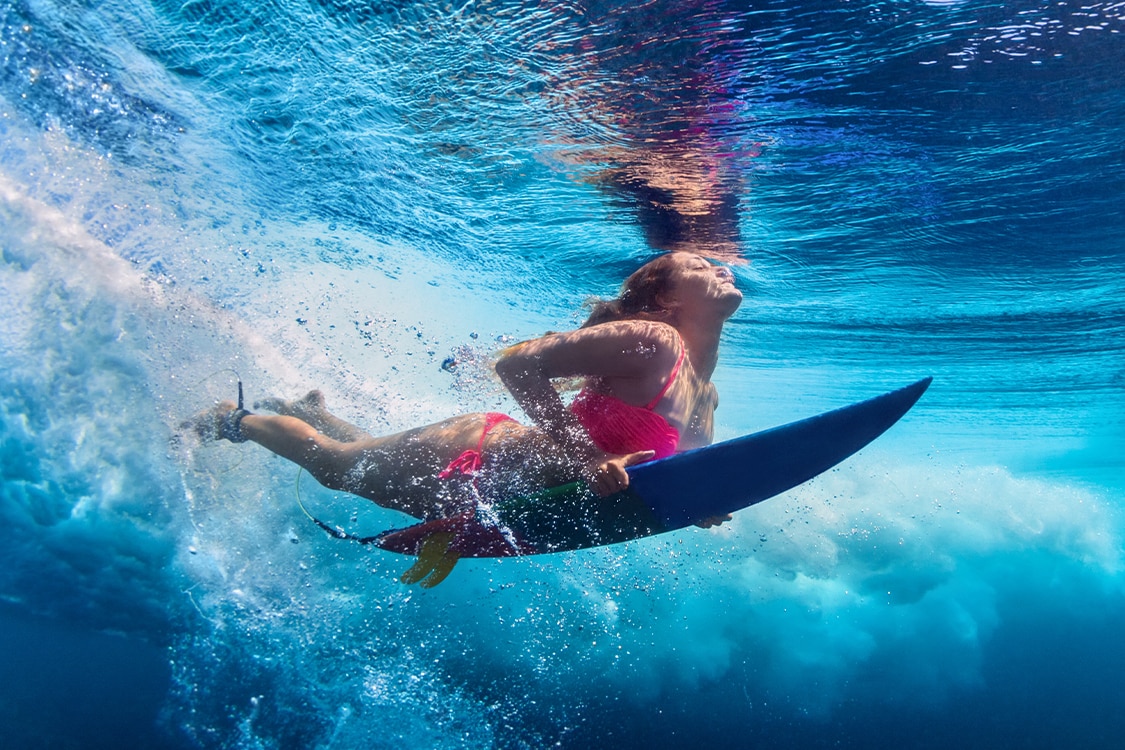 Underwater view of a surfer riding a wave in Maui's clear blue ocean. 