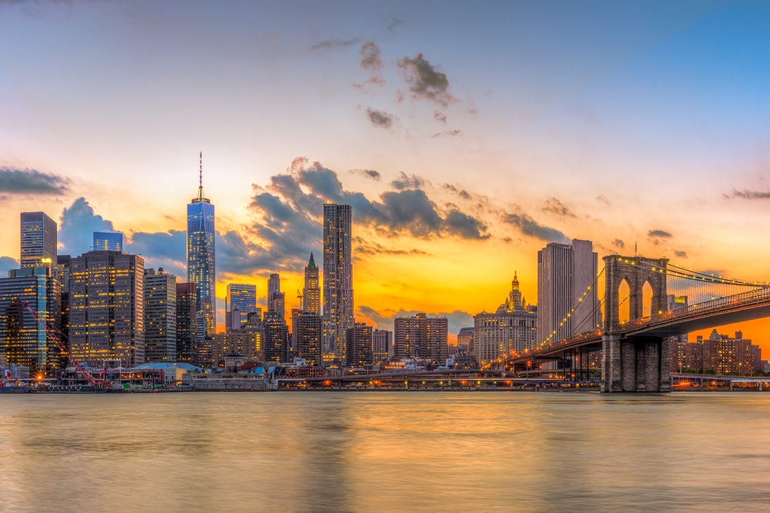 New York City skyline at sunset with Manhattan skyscrapers and the Brooklyn Bridge over the East River.