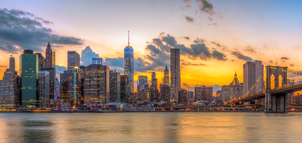 New York City skyline at sunset with Manhattan skyscrapers and the Brooklyn Bridge over the East River.