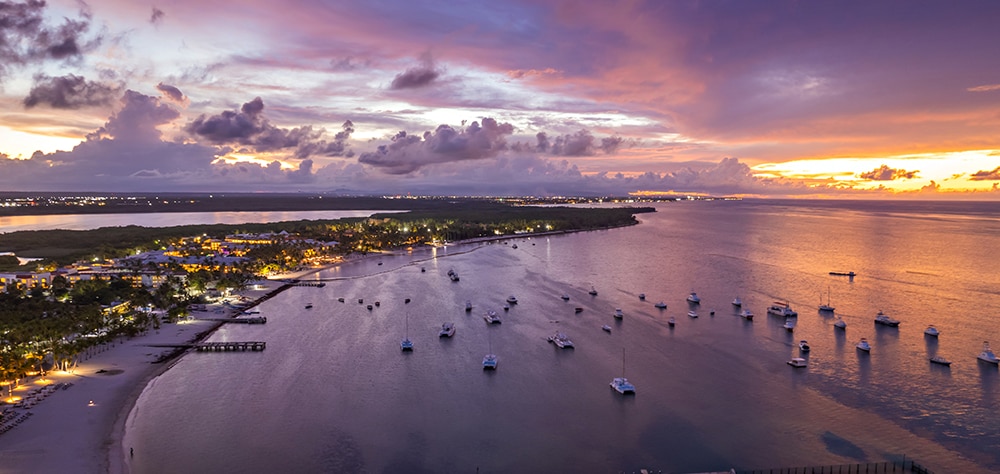 Aerial view of Punta Cana coastline at sunset with boats anchored offshore. 
