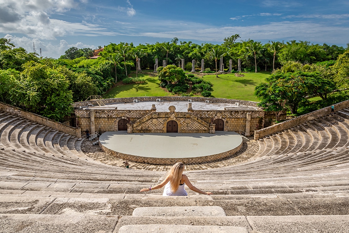 Woman sitting in stone ampitheater surrounded by lush gardens in the Dominican Republic.