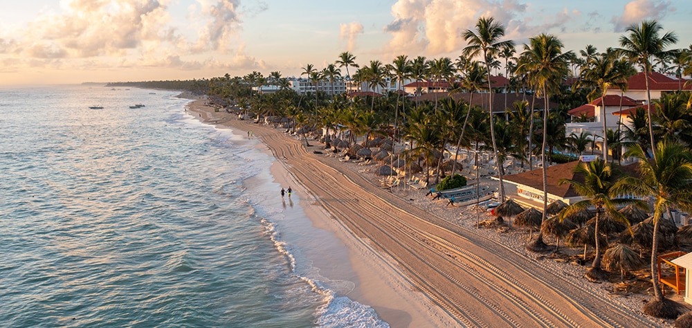 Aerial view of a palm-lined beach and turquoise ocean waters during sunset in Punta Cana. 
