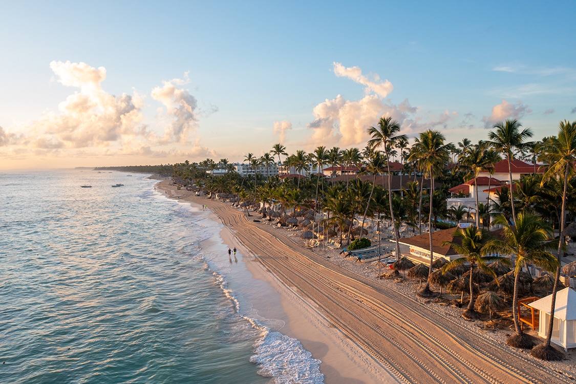 Aerial view of a palm-lined beach and turquoise ocean waters during sunset in Punta Cana. 